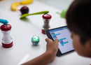 Young boy programming mini robotic ball in between a salt and pepper shaker.