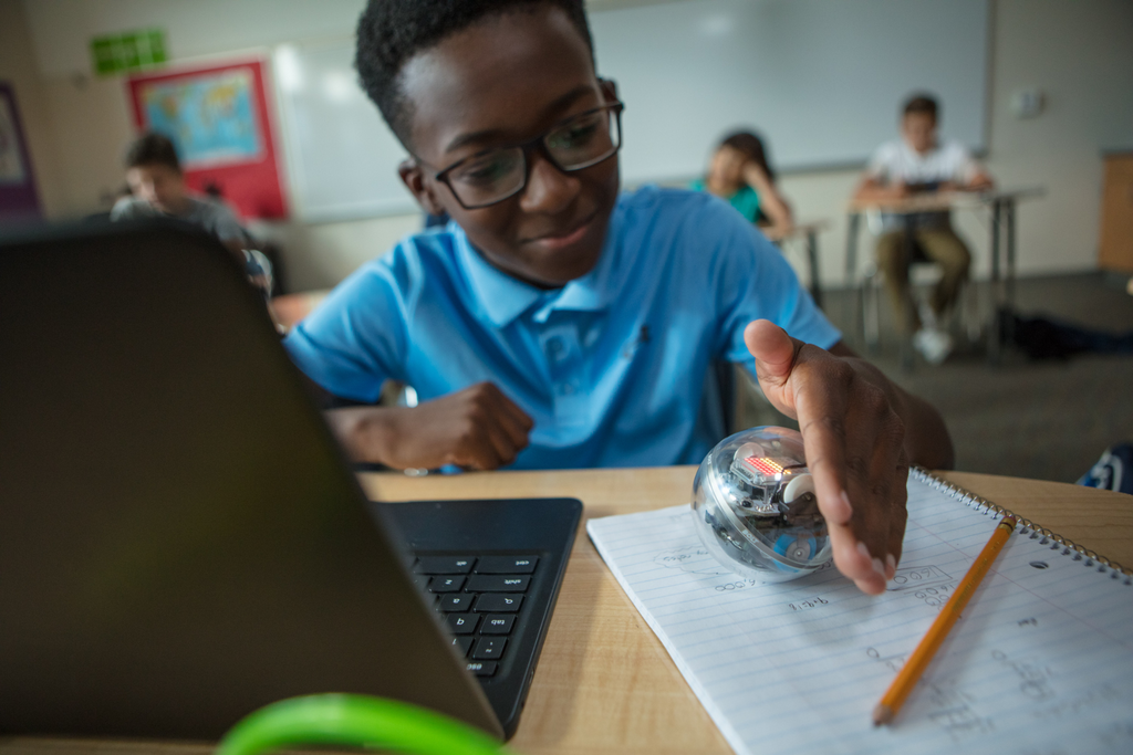 A student looking at a Sphero BOLT on his desk.