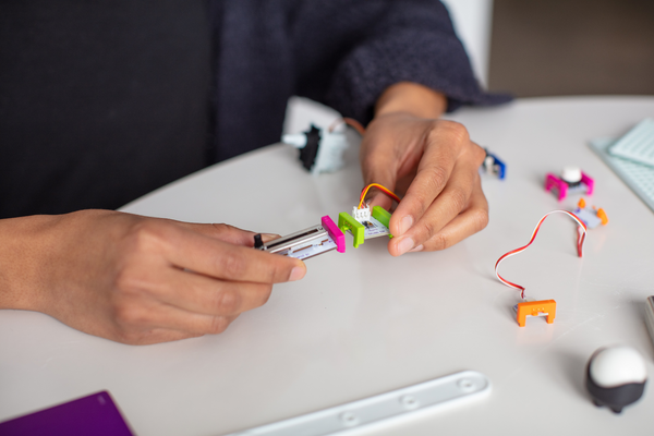 A student's hands connect two littleBits pieces.